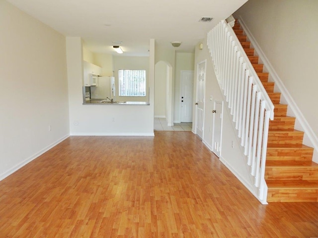 5927 Riverside Ave, Tamarac, FL 33321 - unfurnished living room with light wood-type flooring, stairs, arched walkways, and baseboards