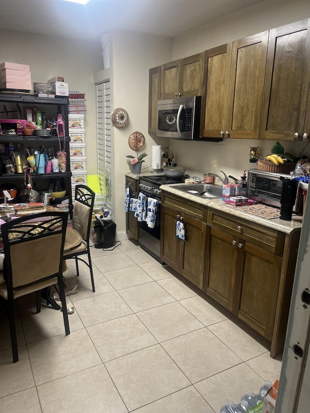 702 48th St, West Palm Beach, FL 33407 - kitchen with stainless steel appliances, a sink, light tile patterned floors, and light countertops