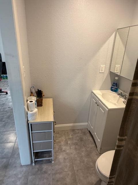 bathroom featuring a textured wall, vanity, toilet, and baseboards