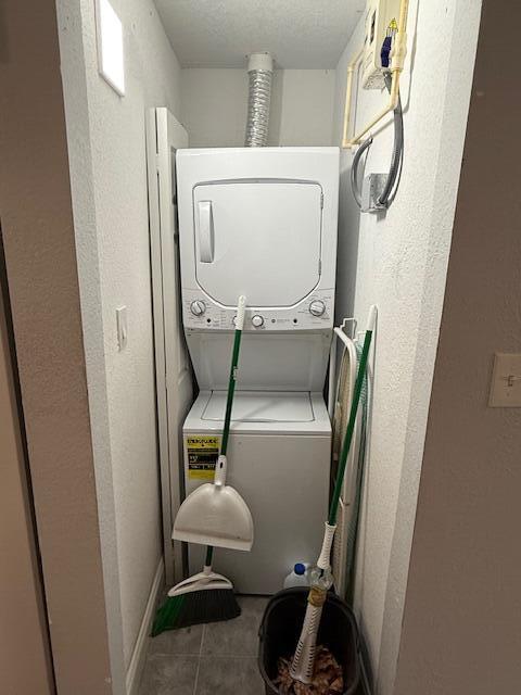 laundry room featuring stacked washing machine and dryer, tile patterned flooring, baseboards, and a textured wall