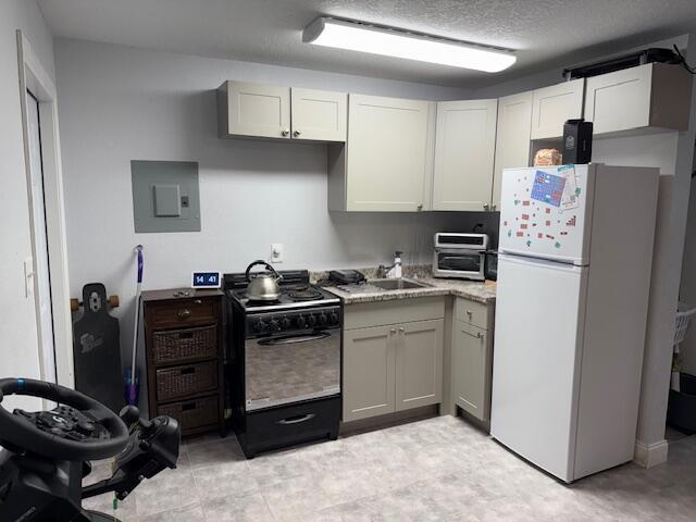 kitchen featuring freestanding refrigerator, black range with gas stovetop, electric panel, and a sink