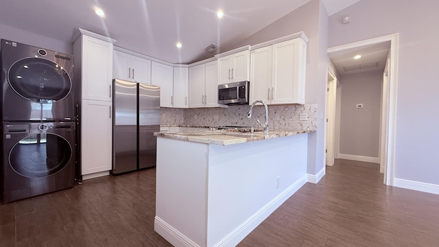 1942 Windsor Dr, North Palm Beach, FL 33408 - kitchen featuring appliances with stainless steel finishes, stacked washer / drying machine, white cabinetry, vaulted ceiling, and decorative backsplash