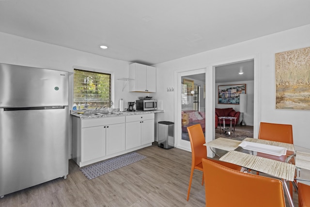 14601 Orange Ave, Fort Pierce, FL 34945 - kitchen featuring appliances with stainless steel finishes, a sink, white cabinets, light wood finished floors, and light stone countertops