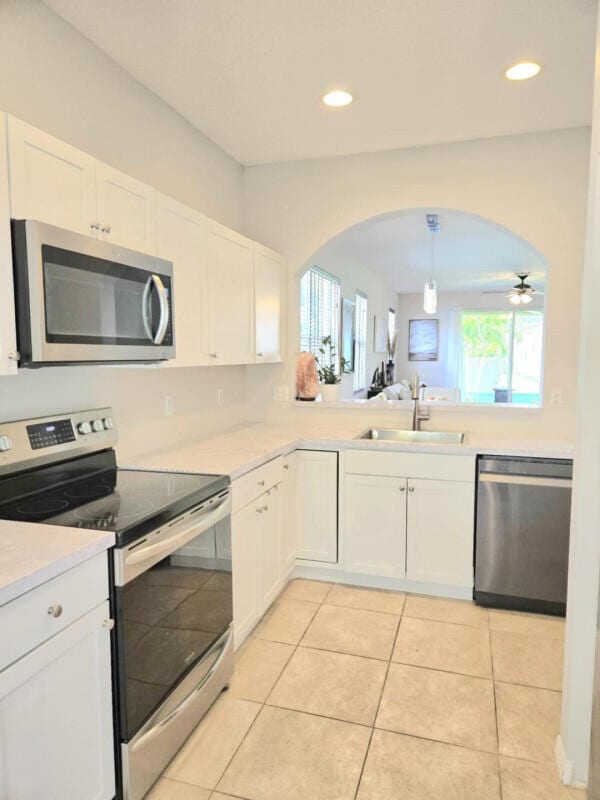 9658 SW Lindale Trace Blvd, Port Saint Lucie, FL 34987 - kitchen with appliances with stainless steel finishes, a sink, arched walkways, light countertops, and white cabinetry