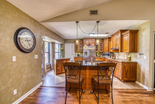11033 67th Pl N, The Acreage, FL 33412 - kitchen featuring a center island with sink, stainless steel appliances, brown cabinets, vaulted ceiling, and light wood-style floors