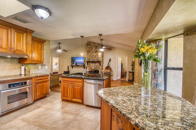 11033 67th Pl N, The Acreage, FL 33412 - kitchen featuring appliances with stainless steel finishes, a ceiling fan, under cabinet range hood, brown cabinets, and dark stone countertops