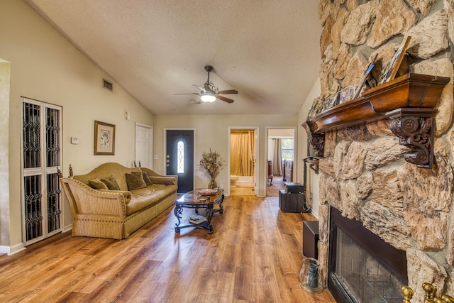 11033 67th Pl N, The Acreage, FL 33412 - living room with a stone fireplace, a textured ceiling, ceiling fan, vaulted ceiling, and wood finished floors
