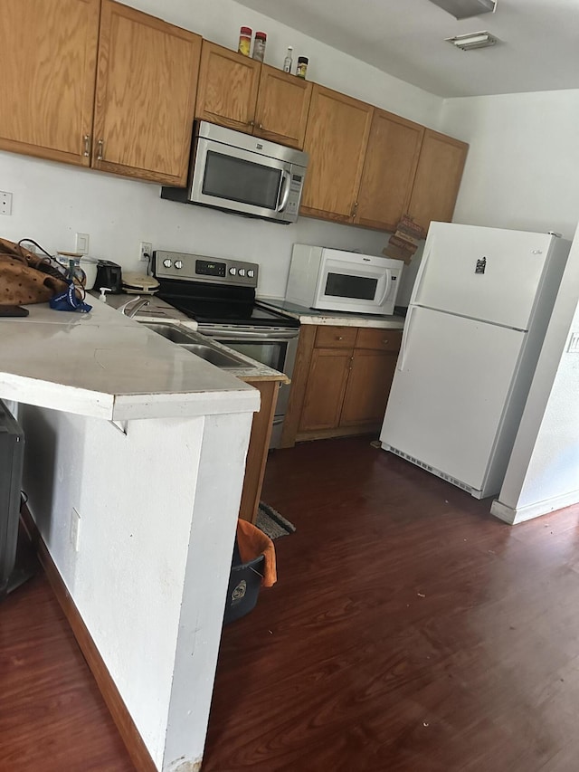 119 S 13th St, Fort Pierce, FL 34950 - kitchen with stainless steel appliances, brown cabinetry, dark wood-style flooring, and a peninsula