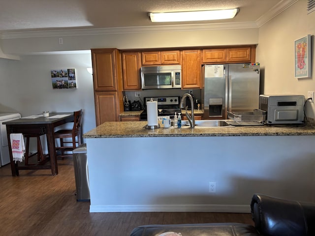 kitchen with appliances with stainless steel finishes, brown cabinetry, dark wood finished floors, ornamental molding, and a peninsula