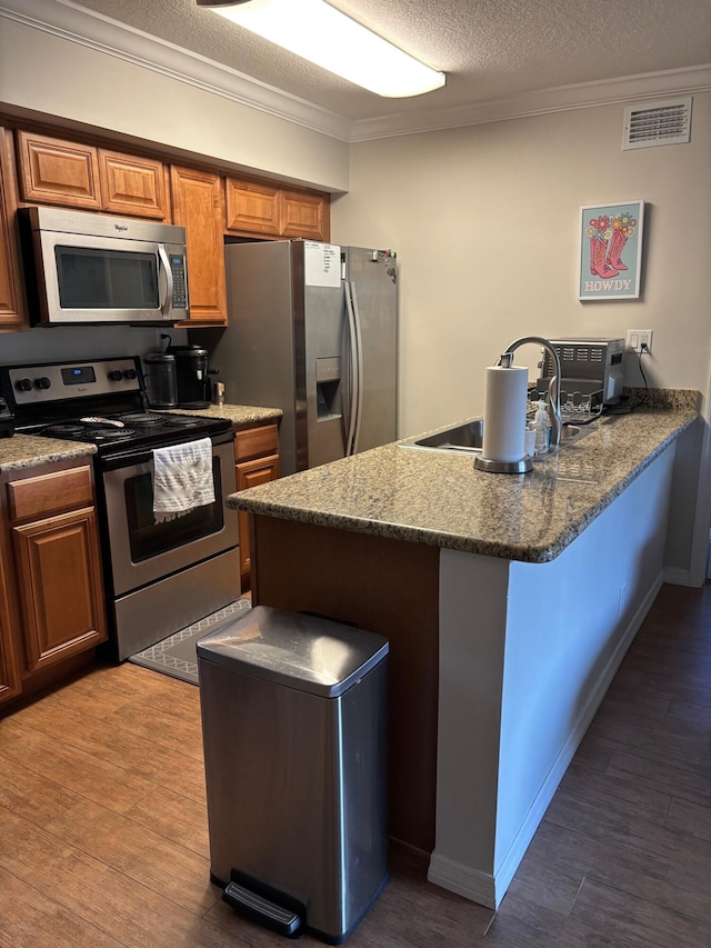 kitchen featuring appliances with stainless steel finishes, a peninsula, crown molding, brown cabinetry, and wood finished floors
