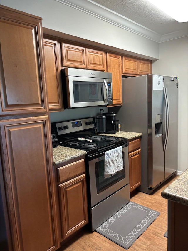 kitchen with stainless steel appliances, crown molding, light wood-type flooring, brown cabinets, and light stone countertops