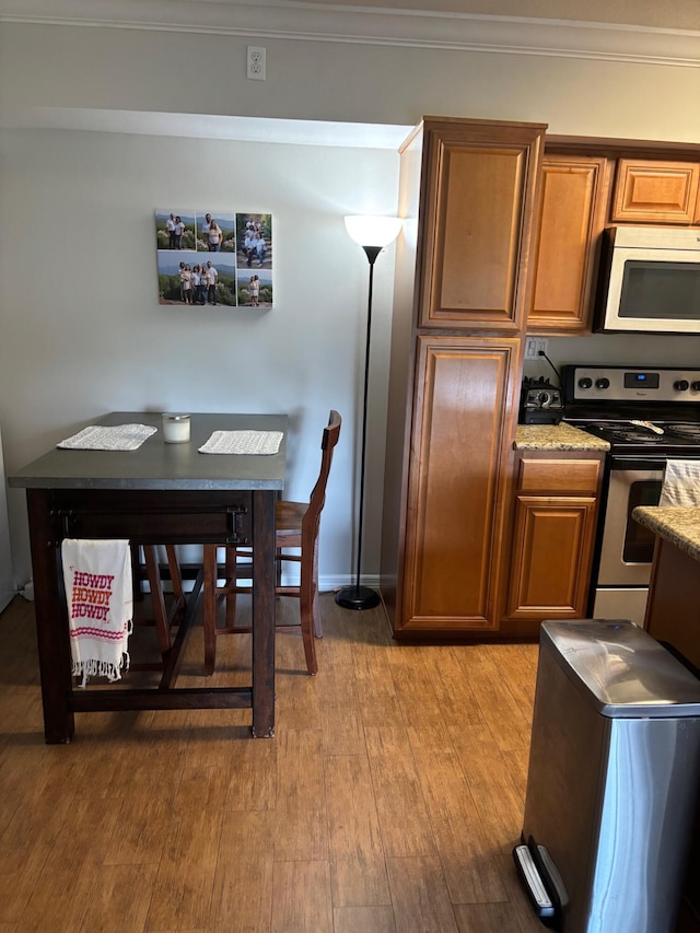 kitchen with stainless steel electric range oven, light wood-style flooring, brown cabinets, ornamental molding, and light stone counters