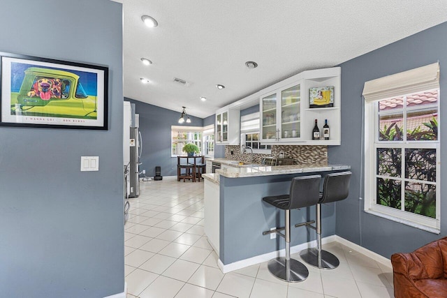 5350 Casa Real Dr, Delray Beach, FL 33484 - kitchen featuring lofted ceiling, a peninsula, glass insert cabinets, light tile patterned floors, and a breakfast bar area