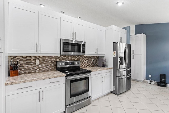 5350 Casa Real Dr, Delray Beach, FL 33484 - kitchen featuring stainless steel appliances, decorative backsplash, white cabinets, light tile patterned floors, and a textured ceiling