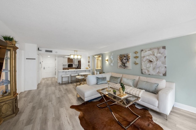 3570 S Ocean Blvd Unit 506, South Palm Beach, FL 33480 - living room featuring light wood finished floors, a textured ceiling, a chandelier, and baseboards