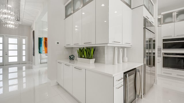13206 Faberge Pl, Palm Beach Gardens, FL 33418 - kitchen featuring stainless steel oven, modern cabinets, beverage cooler, a chandelier, and white cabinetry