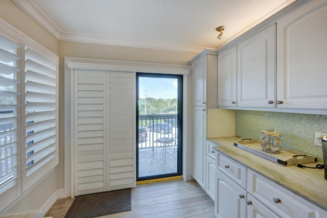 2641 NE Ocean Blvd Unit 106, Stuart, FL 34996 - kitchen featuring decorative backsplash, light wood-style flooring, light stone countertops, ornamental molding, and white cabinetry