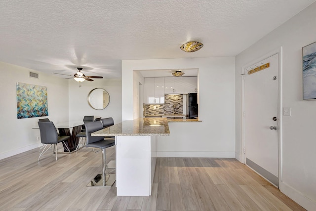 3640 N Ocean Dr Unit 427, Singer Island, FL 33404 - kitchen featuring white cabinetry, backsplash, light stone countertops, a breakfast bar, and a peninsula