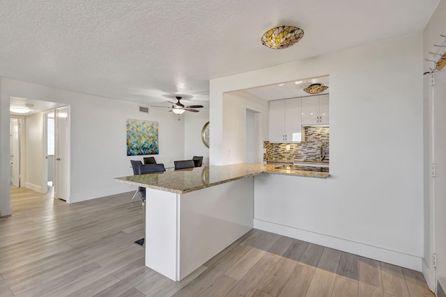 3640 N Ocean Dr Unit 427, Singer Island, FL 33404 - kitchen featuring white cabinetry, a ceiling fan, light wood-type flooring, a peninsula, and tasteful backsplash