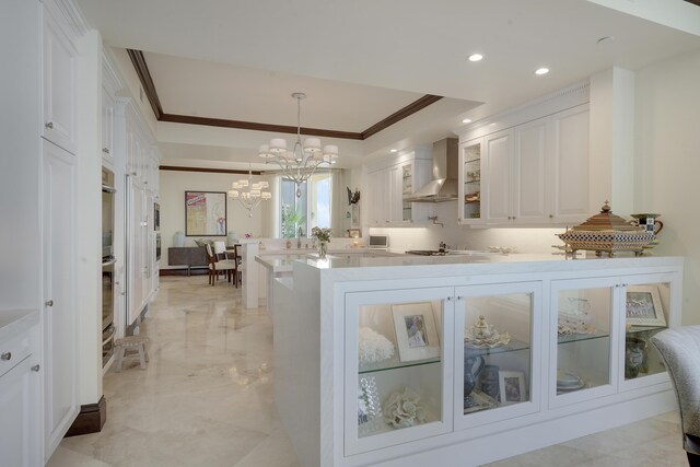 5050 N Ocean Dr Unit 1701, Singer Island, FL 33404 - kitchen featuring wall chimney range hood, crown molding, a peninsula, a chandelier, and white cabinetry