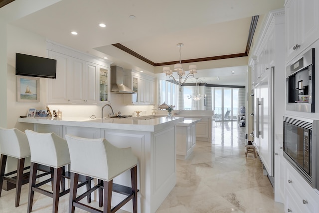 5050 N Ocean Dr Unit 1701, Singer Island, FL 33404 - kitchen featuring wall chimney range hood, built in appliances, a peninsula, ornamental molding, and a chandelier