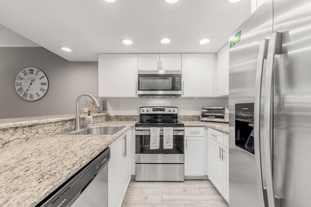 390 NE Edgewater Dr Unit 302, Stuart, FL 34996 - kitchen featuring stainless steel appliances, a sink, white cabinets, backsplash, and light stone countertops