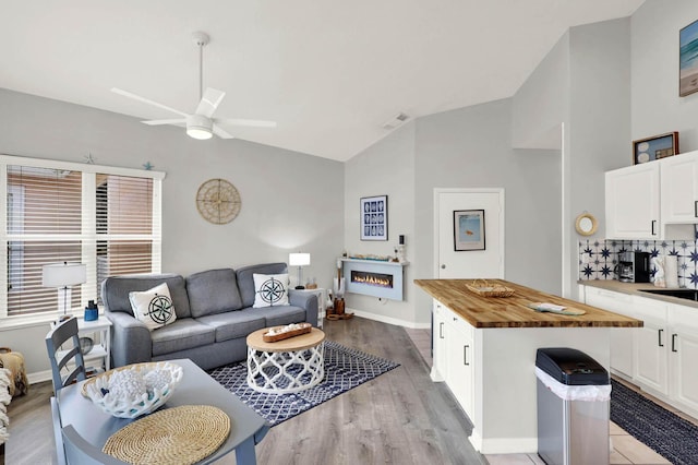 9927 Perfect Dr Unit 108, Port Saint Lucie, FL 34986 - living room featuring a ceiling fan, a lit fireplace, light wood-type flooring, baseboards, and high vaulted ceiling