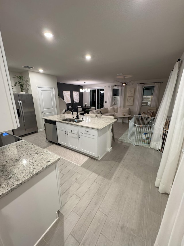 5700 Mentmore Dr, Mangonia Park, FL 33407 - kitchen with stainless steel appliances, a sink, white cabinets, light wood-type flooring, and a center island with sink