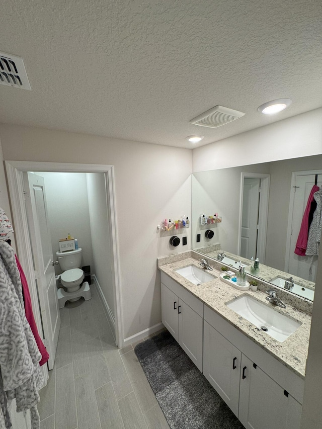 5700 Mentmore Dr, Mangonia Park, FL 33407 - full bath featuring toilet, a textured ceiling, baseboards, and double vanity