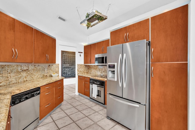 498 Oregon Ln, Boca Raton, FL 33487 - kitchen with stainless steel appliances, decorative backsplash, light tile patterned floors, brown cabinetry, and light stone countertops