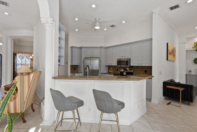 1936 SW Wood Duck Ln, Palm City, FL 34990 - kitchen featuring appliances with stainless steel finishes, ornate columns, a ceiling fan, a peninsula, and stone counters