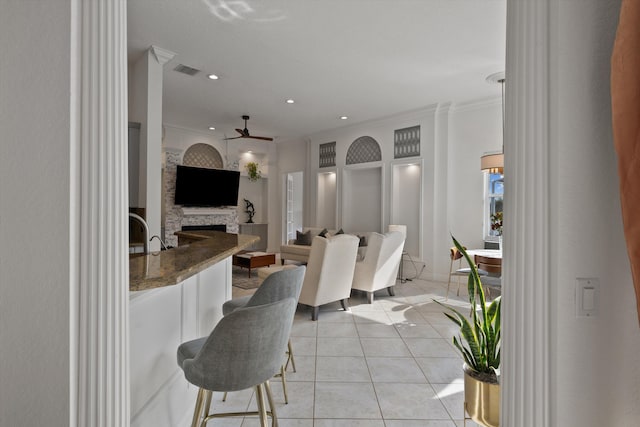 1936 SW Wood Duck Ln, Palm City, FL 34990 - kitchen featuring a ceiling fan, light tile patterned floors, a fireplace, a kitchen breakfast bar, and ornamental molding