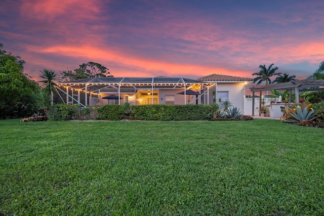 1936 SW Wood Duck Ln, Palm City, FL 34990 - back of property at dusk featuring a yard, stucco siding, a tiled roof, and glass enclosure