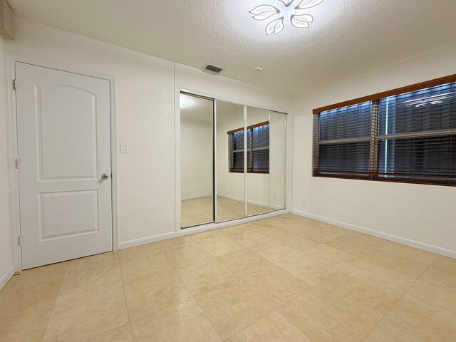 1034 Almeria Rd, West Palm Beach, FL 33405 - unfurnished bedroom featuring a textured ceiling, baseboards, a closet, and light tile patterned floors