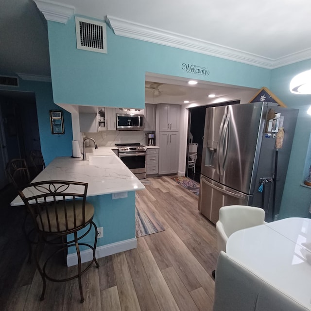 54 Piedmont Unit B, Delray Beach, FL 33484 - kitchen with appliances with stainless steel finishes, crown molding, a peninsula, a breakfast bar area, and light wood-type flooring