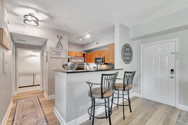 804 E Windward Way Unit 404, Lantana, FL 33462 - kitchen with stainless steel appliances, light wood-type flooring, decorative backsplash, a breakfast bar area, and dark countertops