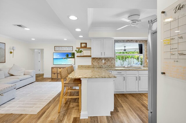 769 Berkeley St, Boca Raton, FL 33487 - kitchen featuring ornamental molding, white cabinets, light wood-style floors, a breakfast bar area, and open floor plan