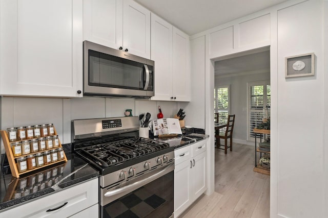 2948 SE Treasure Island Rd, Port Saint Lucie, FL 34952 - kitchen featuring appliances with stainless steel finishes, white cabinets, dark stone countertops, and light wood-type flooring