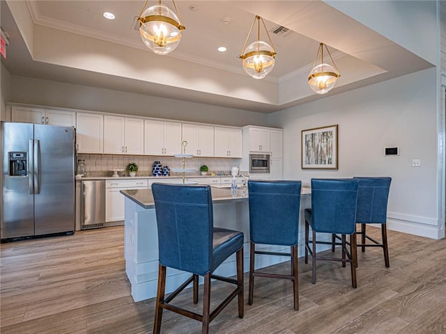 1095 N Verona Trace Dr, Vero Beach, FL 32966 - kitchen featuring stainless steel appliances, a raised ceiling, ornamental molding, light wood-type flooring, and white cabinetry
