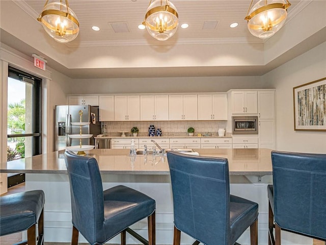 1095 N Verona Trace Dr, Vero Beach, FL 32966 - kitchen with stainless steel appliances, a raised ceiling, backsplash, white cabinets, and ornamental molding
