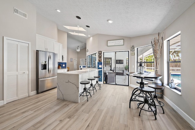 407 SE Duff Ct, Port Saint Lucie, FL 34984 - kitchen with stainless steel fridge, light wood-type flooring, a textured ceiling, a kitchen breakfast bar, and white cabinets