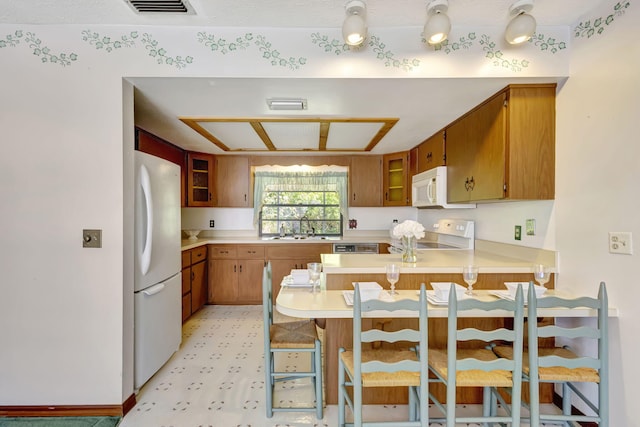 102 SE Crosspoint Dr, Port Saint Lucie, FL 34983 - kitchen with white appliances, a peninsula, a sink, light countertops, and brown cabinetry