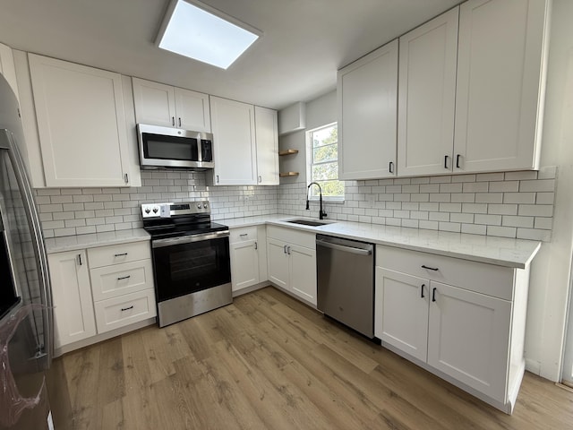 711 NW Riverside Dr, Port Saint Lucie, FL 34983 - kitchen featuring appliances with stainless steel finishes, a sink, open shelves, light wood finished floors, and white cabinets