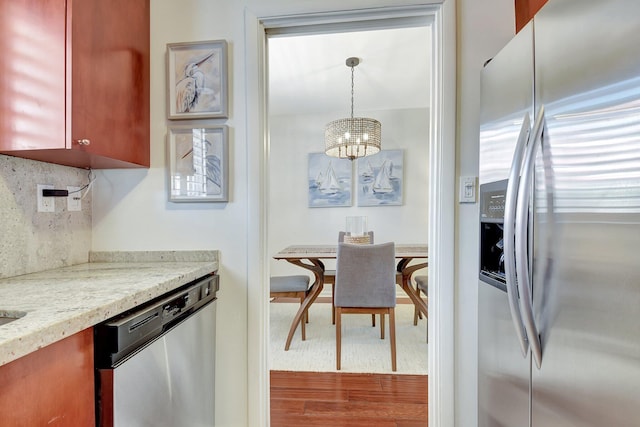426 NE 7th Ave Unit 1F, Delray Beach, FL 33483 - kitchen with appliances with stainless steel finishes, a chandelier, wood finished floors, backsplash, and light stone countertops