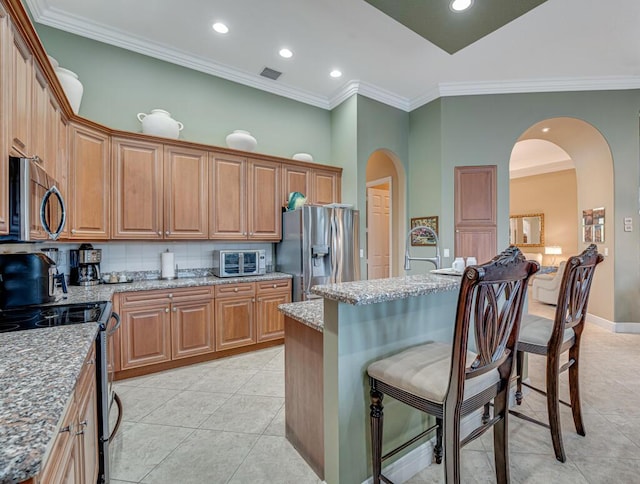 1885 Via Bellezza, Wellington, FL 33411 - kitchen with stainless steel appliances, a kitchen breakfast bar, light tile patterned floors, light stone counters, and arched walkways