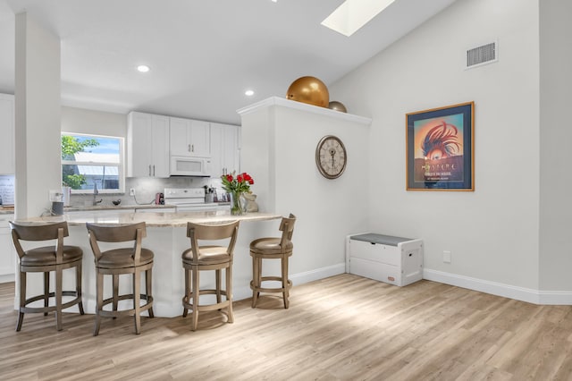 6304 SE Ames Way, Hobe Sound, FL 33455 - kitchen featuring white appliances, a skylight, backsplash, a breakfast bar area, and light wood-style flooring