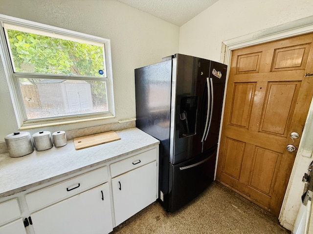 3901 Neptune Dr SE, Saint Petersburg, FL 33705 - kitchen featuring black fridge, light countertops, plenty of natural light, white cabinets, and a textured ceiling