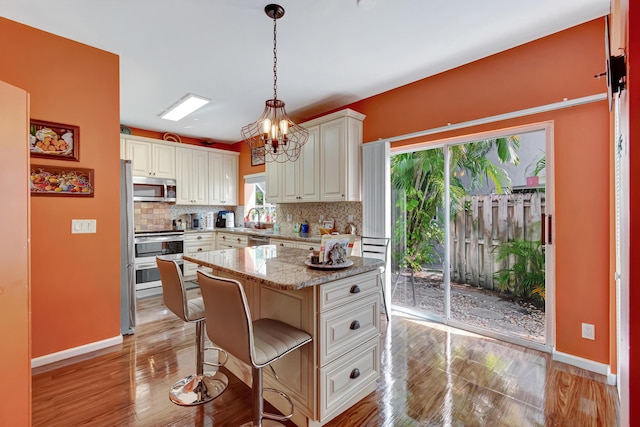 11650 Briarwood Cir Unit 2, Boynton Beach, FL 33437 - kitchen featuring appliances with stainless steel finishes, decorative backsplash, a kitchen breakfast bar, baseboards, and light wood-style flooring