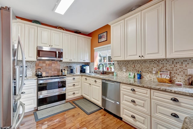 11650 Briarwood Cir Unit 2, Boynton Beach, FL 33437 - kitchen featuring appliances with stainless steel finishes, a sink, backsplash, light wood-type flooring, and light stone counters