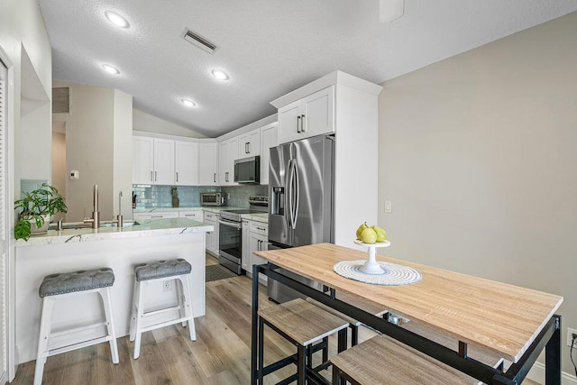 10560 Plainview Cir, Boca Raton, FL 33498 - kitchen featuring stainless steel appliances, lofted ceiling, decorative backsplash, white cabinets, and light wood finished floors